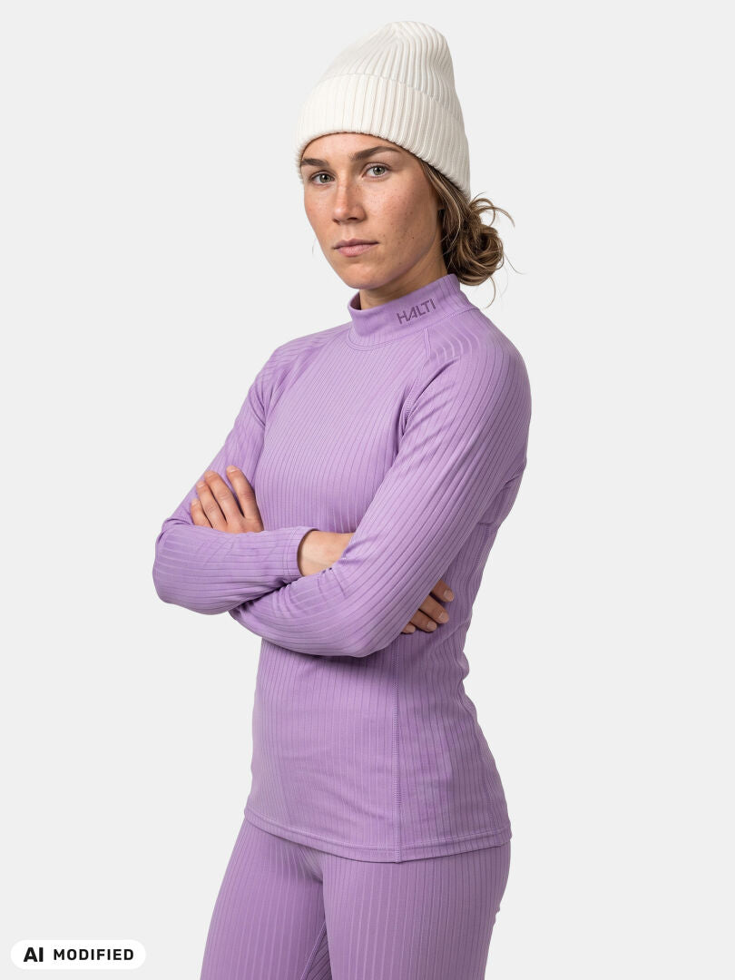 Person in einem violetten „Halti Dual Baselayer Set Damen“ aus recyceltem Polyester, mit weißer Strickmütze, die Arme verschränkt.