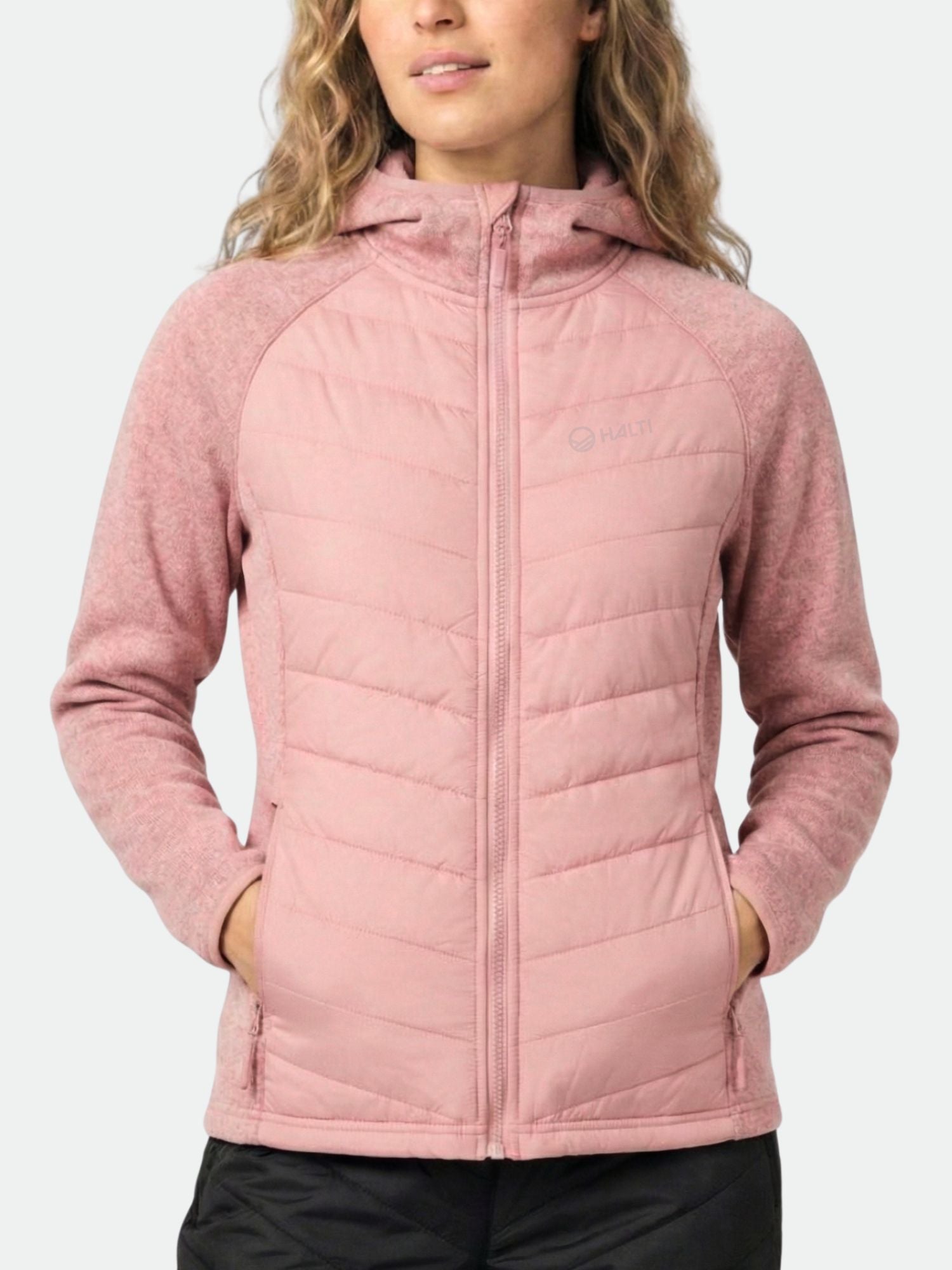 Eine Frau in einer hellrosa Halti Streams Hybrid Midlayer Jacke Damen, ideal für Outdoor-Aktivitäten.