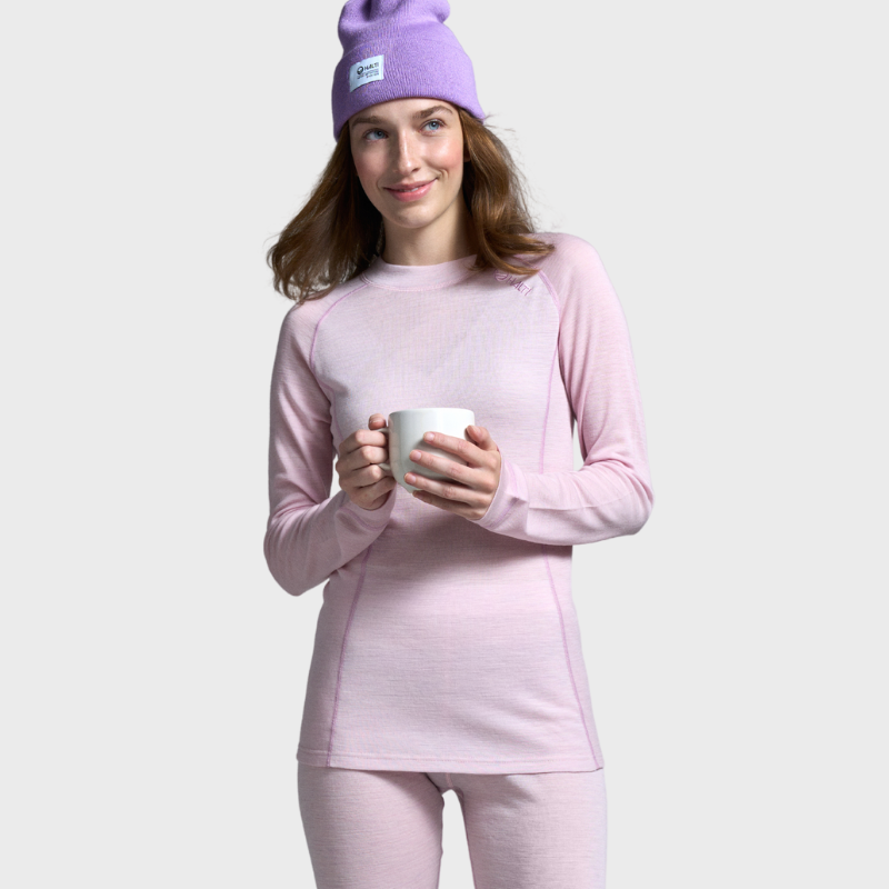 Eine Frau im Halti Hossa Merino Unterwäsche-Set für Damen und einer lila Mütze hält einen Becher und ist bereit für Spaß im Freien.