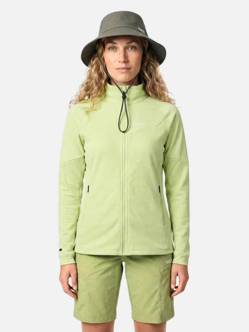 Eine Person in einer Halti HeatGrid Midlayer Jacke Damen, passenden Shorts und grauer Mütze steht mit dem Gesicht nach vorne.