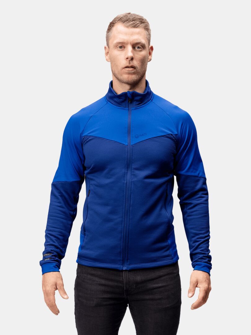 Ein Mann trägt die Halti HeatGrid Midlayer Jacke Herren, die Wärme und Bewegungsfreiheit aus recyceltem Polyester bietet.