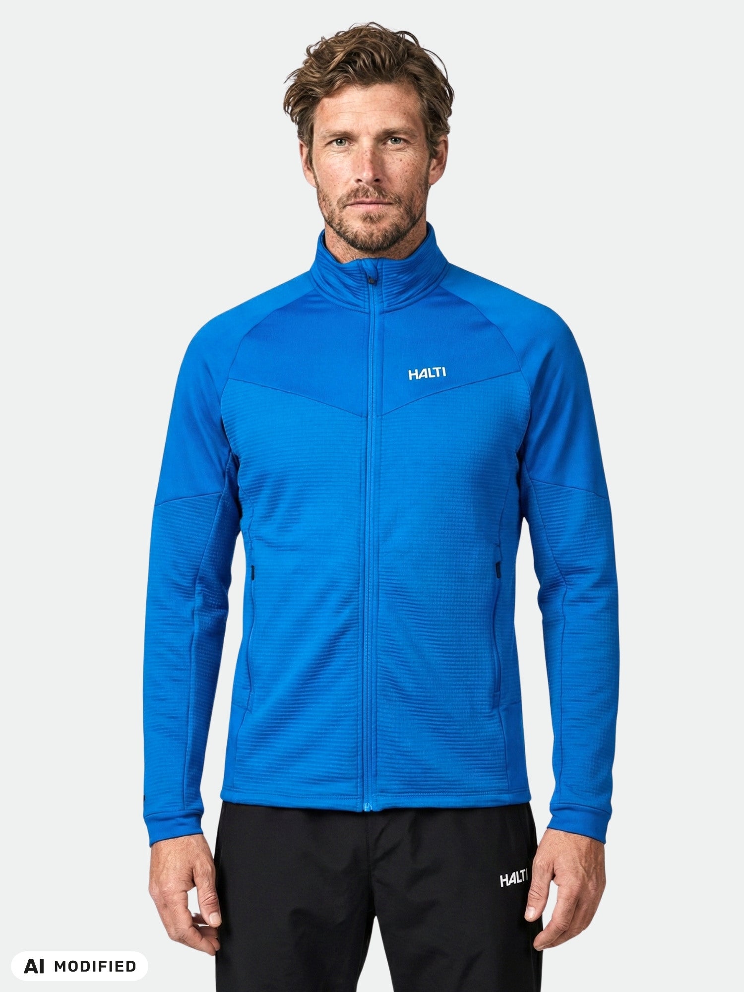 Mann in einer blauen Halti HeatGrid Midlayer-Jacke aus recyceltem Polyester, die Wärme und Bewegungsfreiheit bietet, im Vordergrund.
