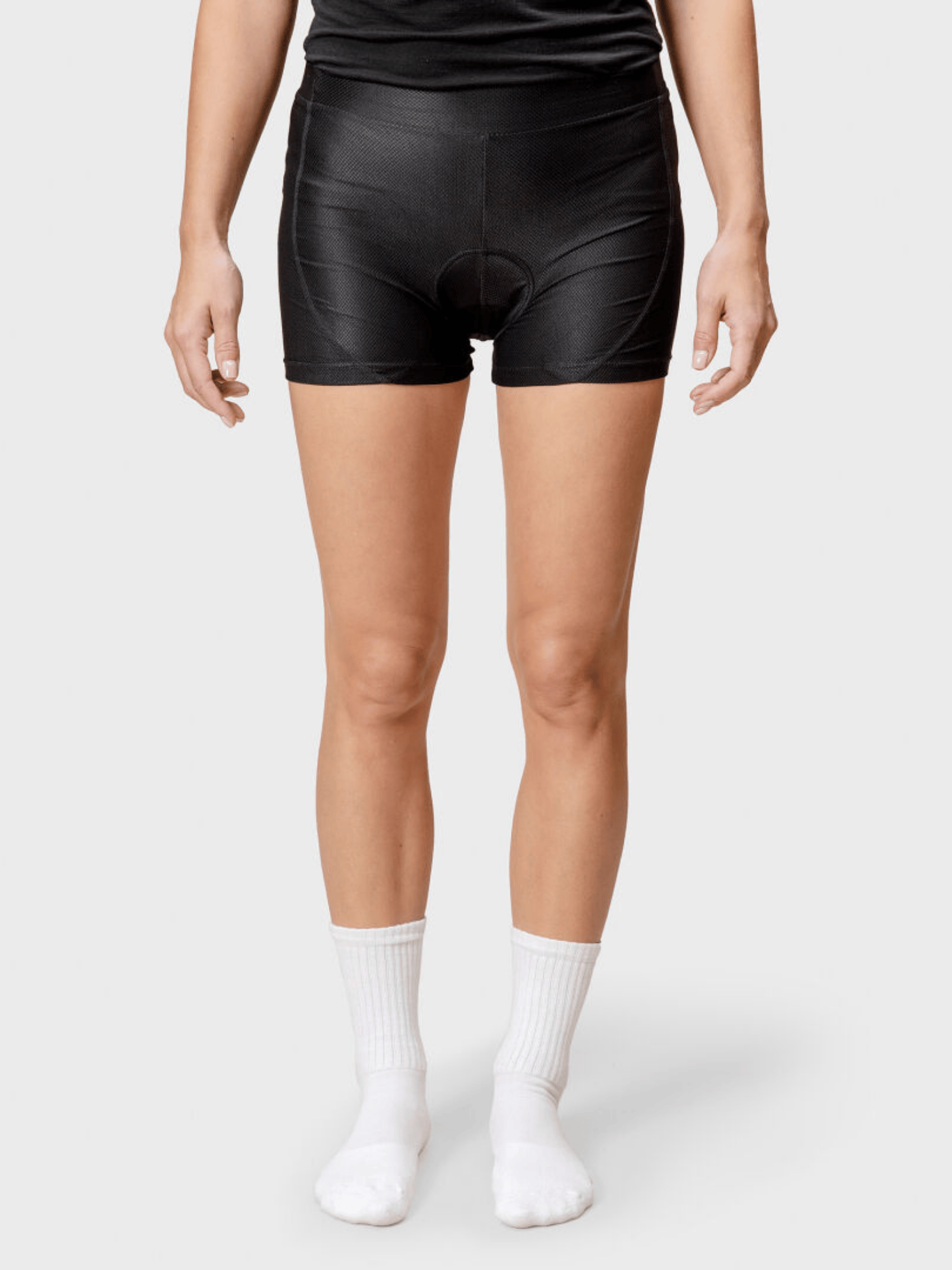 Stehende Person, die schwarze Halti Bike Rad Shorts Damen, weiße Socken und ein schwarzes Shirt vor einem hellen Hintergrund trägt.