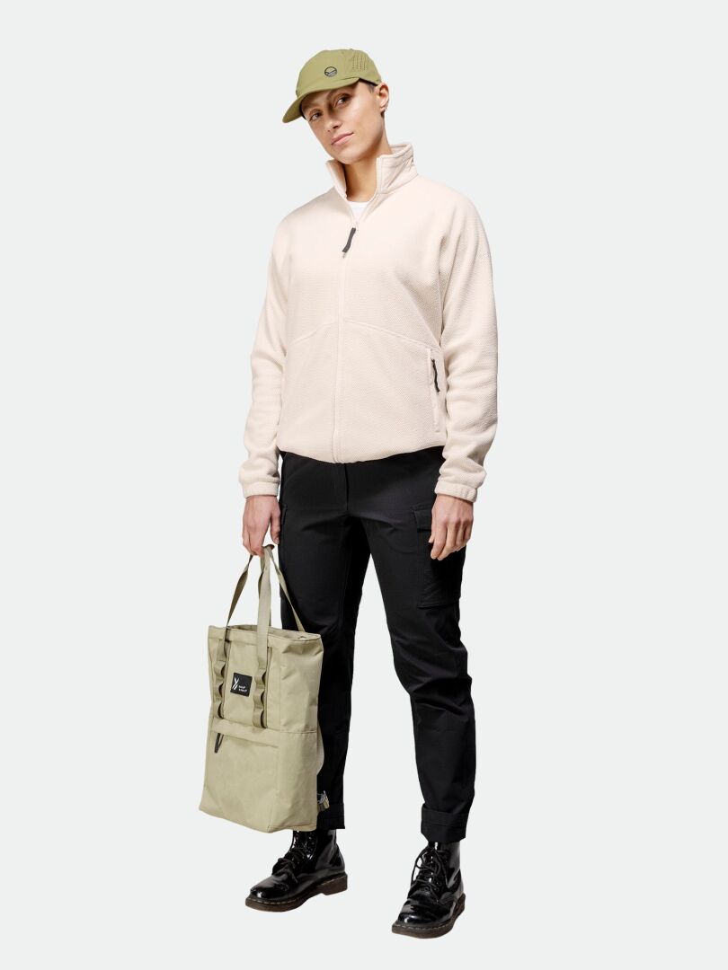 Die Person trägt eine Halti Soolo Midlayer Jacke Damen, eine schwarze Hose und Schuhe, eine grüne Mütze und eine hellgrüne Tragetasche.