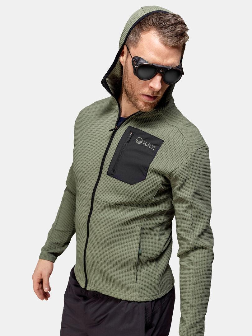 Links steht ein Mann in einer Halti Ultramove Midlayer Jacke für Herren mit 3D-Strick-Aktivjersey und trägt eine Sonnenbrille.