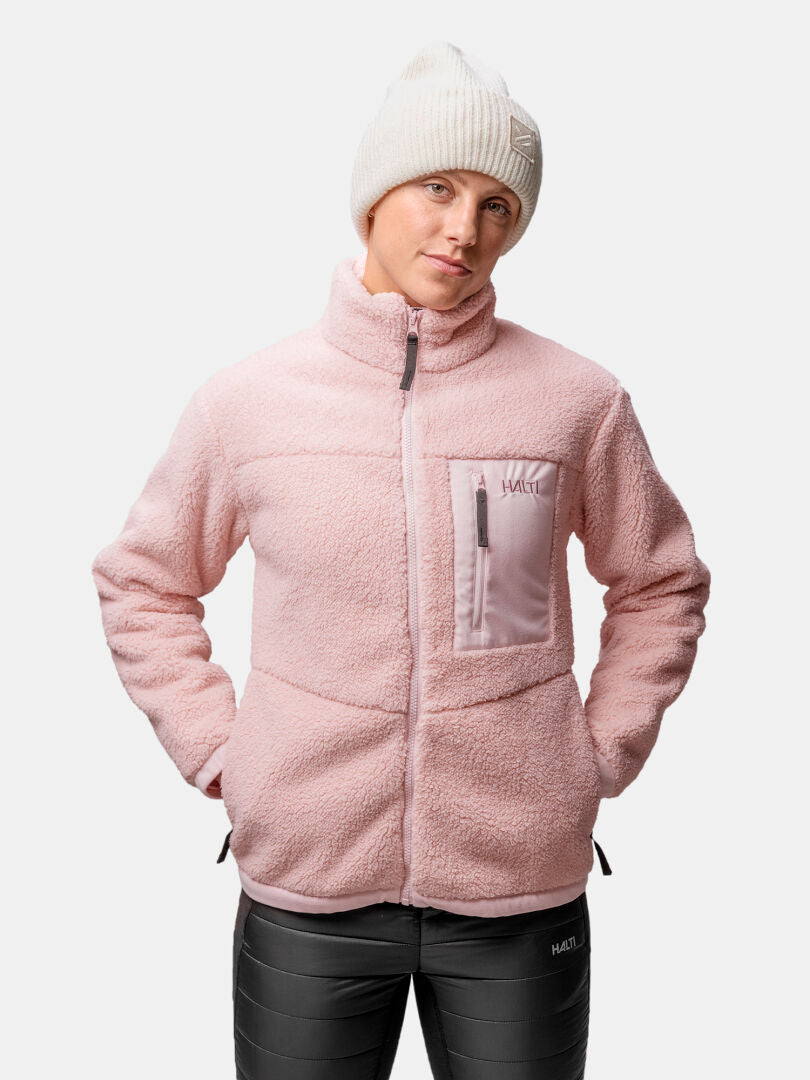 Frau in einer Halti Lumista Polar-Fleecejacke und einer weißen Mütze, winddicht, bereit zum Wandern vor einem neutralen Hintergrund.