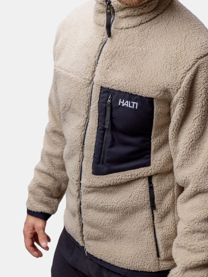 Ein Mann trägt eine Halti Lumista Polar Fleece Jacke Herren mit schwarzen Reißverschlusstaschen und Halti Branding auf der Brust.