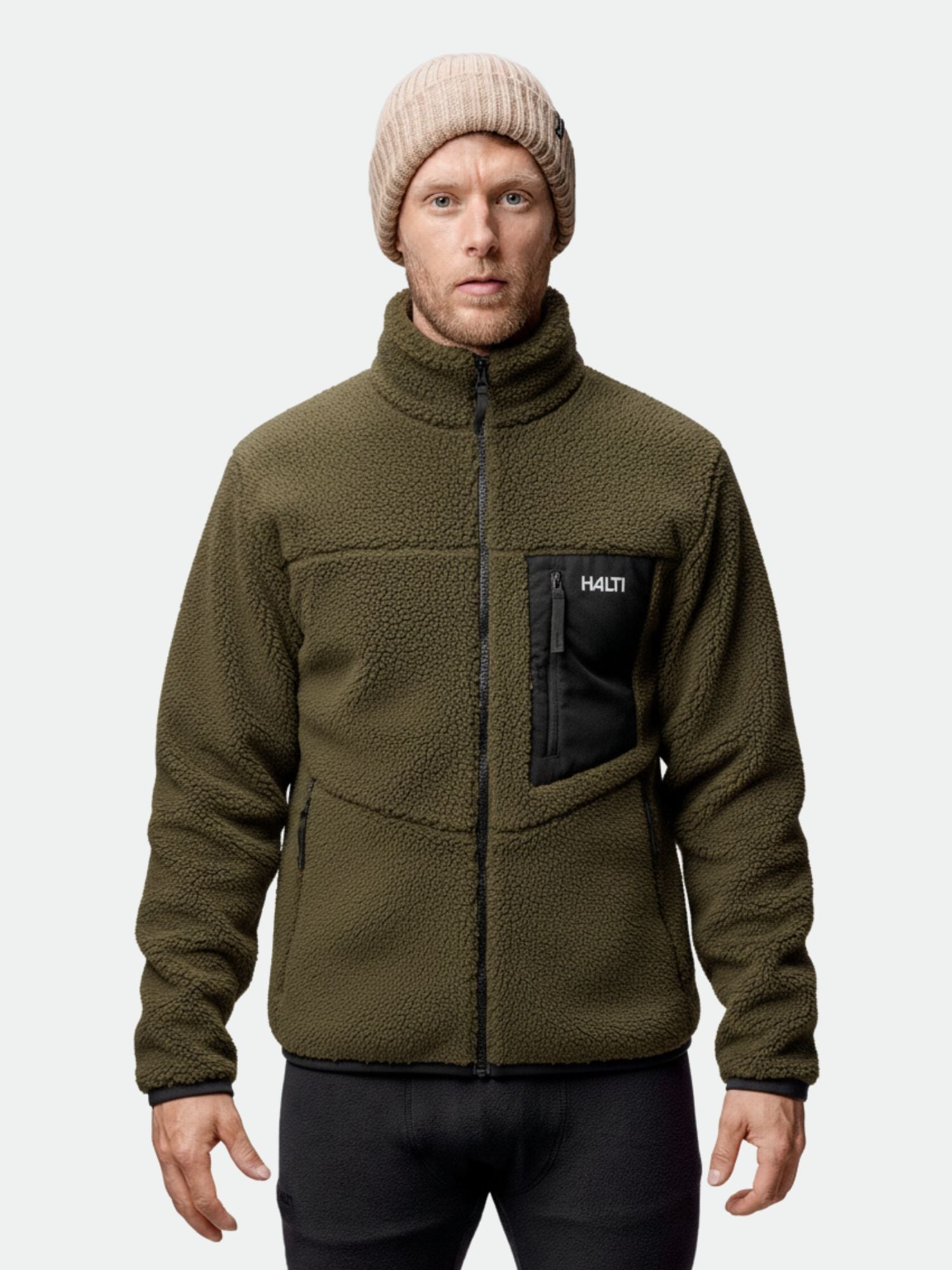 Ein Mann in einer Halti Lumista Polar Fleece Jacke Herren und beiger Strickmütze blickt vor einem schlichten Hintergrund in die Kamera.