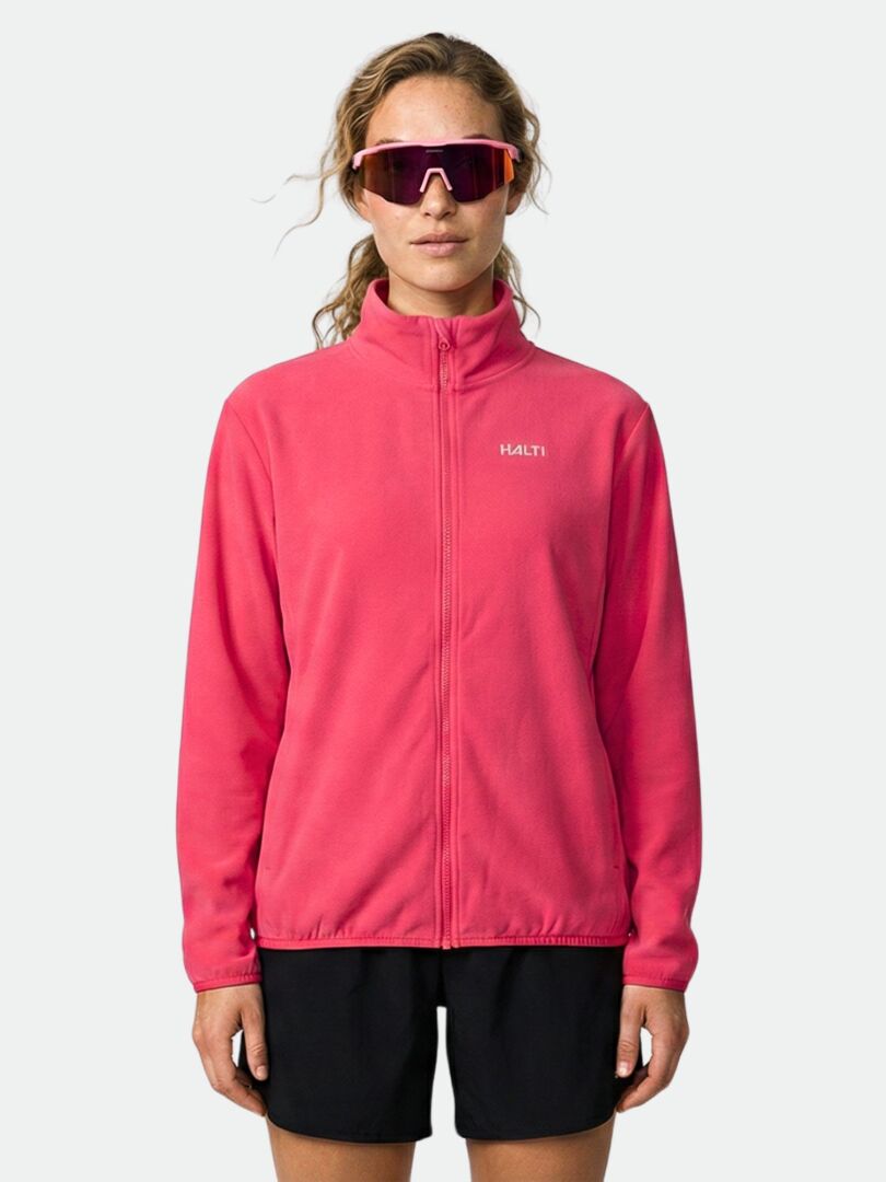 Eine Person in einer rosa Halti Rockmoon Fleecejacke Damen, schwarzen Shorts und einer großen rosa Sonnenbrille steht mit dem Gesicht nach vorne.