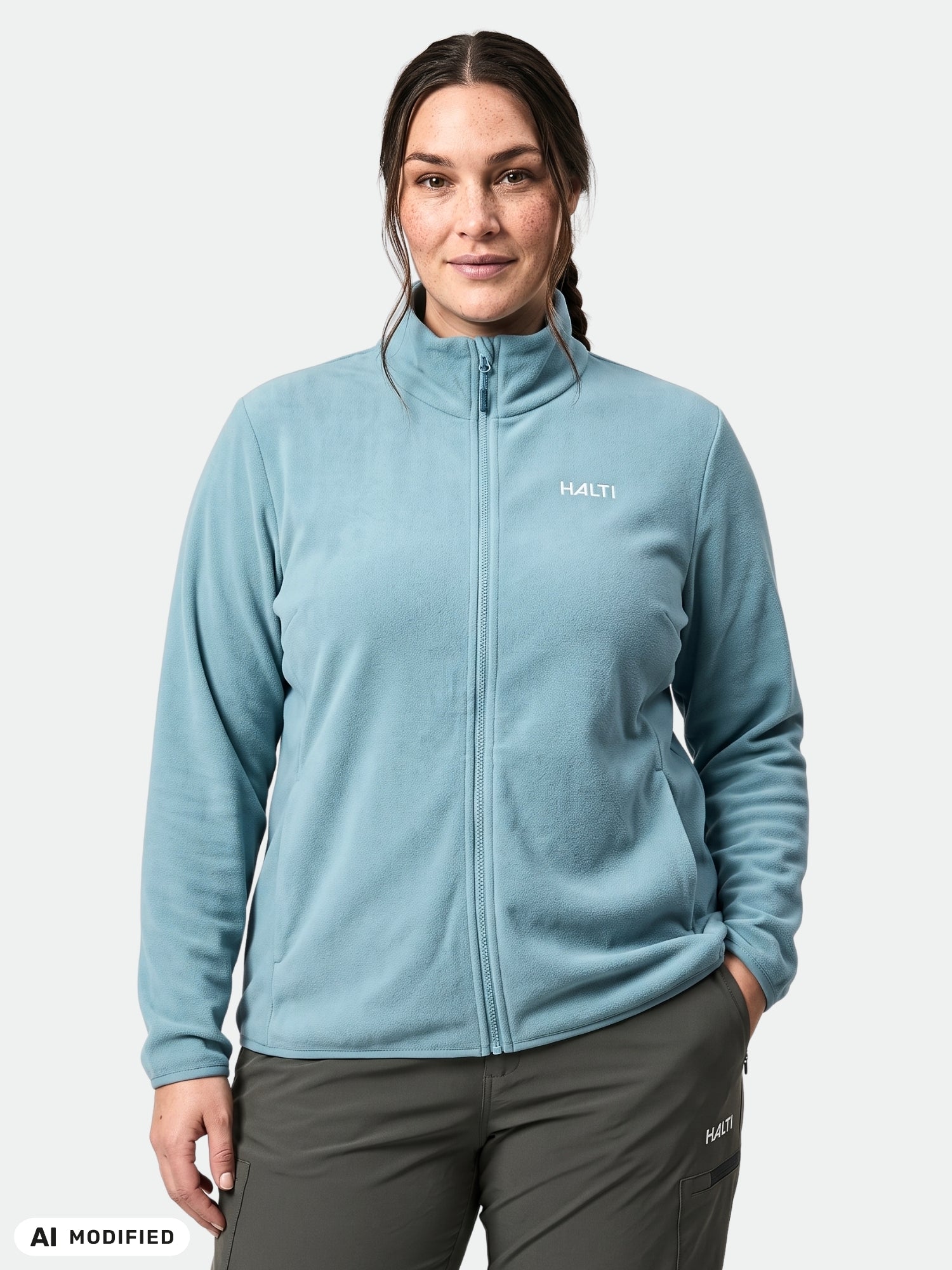 Eine Frau trägt eine Halti Rockmoon Fleecejacke für Damen in Größe Plus in Hellblau und eine graue Hose vor einem weißen Hintergrund.