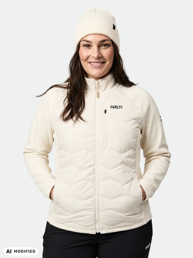 Eine Person trägt eine cremefarbene Halti Suomis Hybrid Layer Jacke Damen Plus mit gestepptem Vorderteil und einer dazu passenden Mütze.