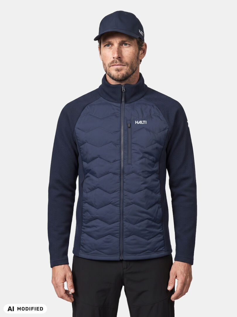 Vor einem einfarbigen Hintergrund steht ein Mann, der eine „Halti Suomis Hybrid Layer Jacke Herren“ und eine Mütze trägt und bereit für Outdoor-Aktivitäten ist.