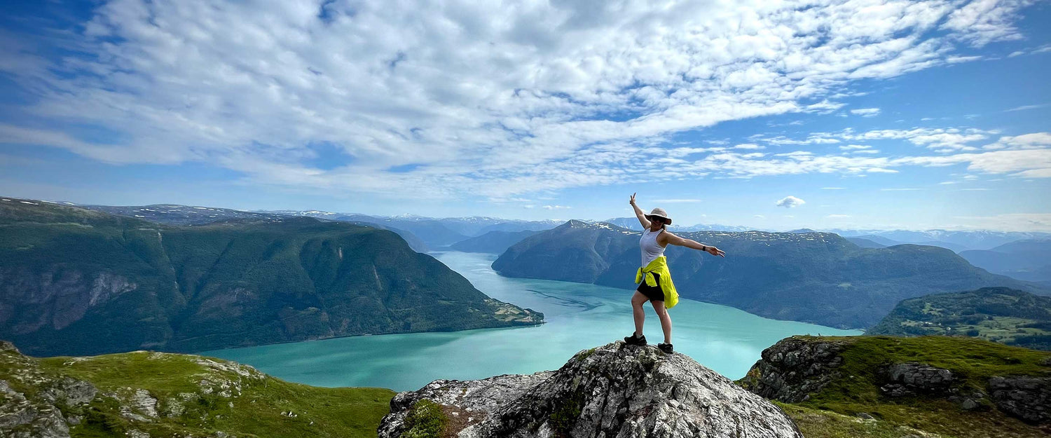 Eine Person steht auf einer felsigen Klippe mit Blick auf einen Fluss und Berge unter einem teilweise bewölkten Himmel.