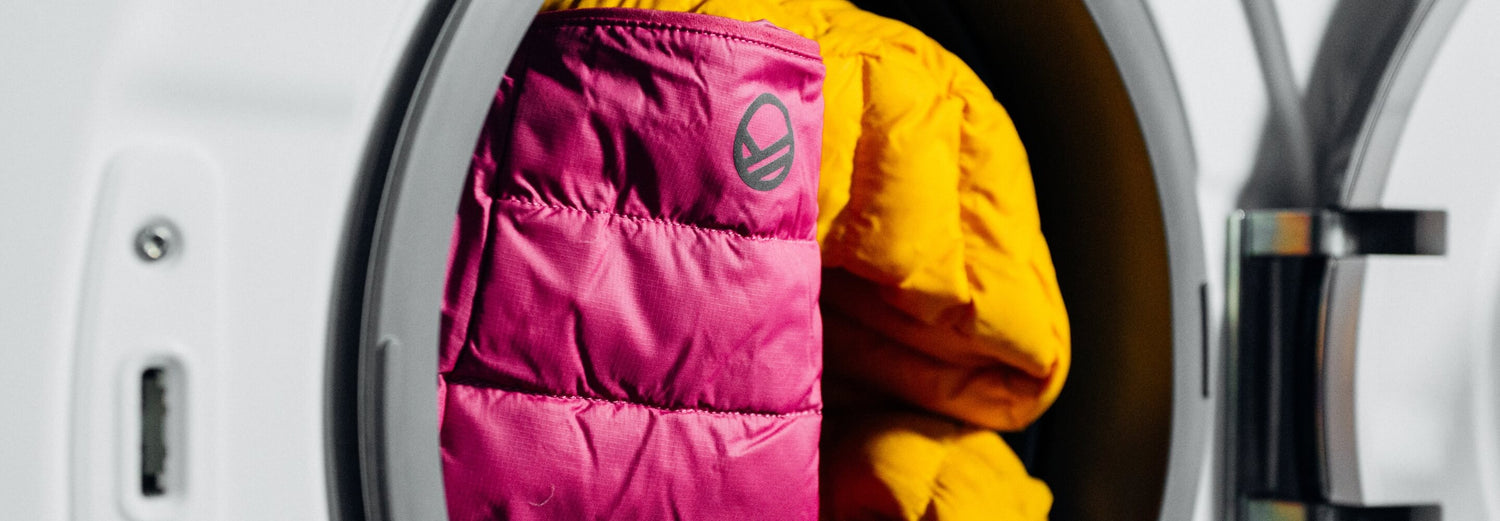 Eine rosa-gelbe Pufferjacke liegt teilweise in der geöffneten Tür einer Frontlader-Waschmaschine.