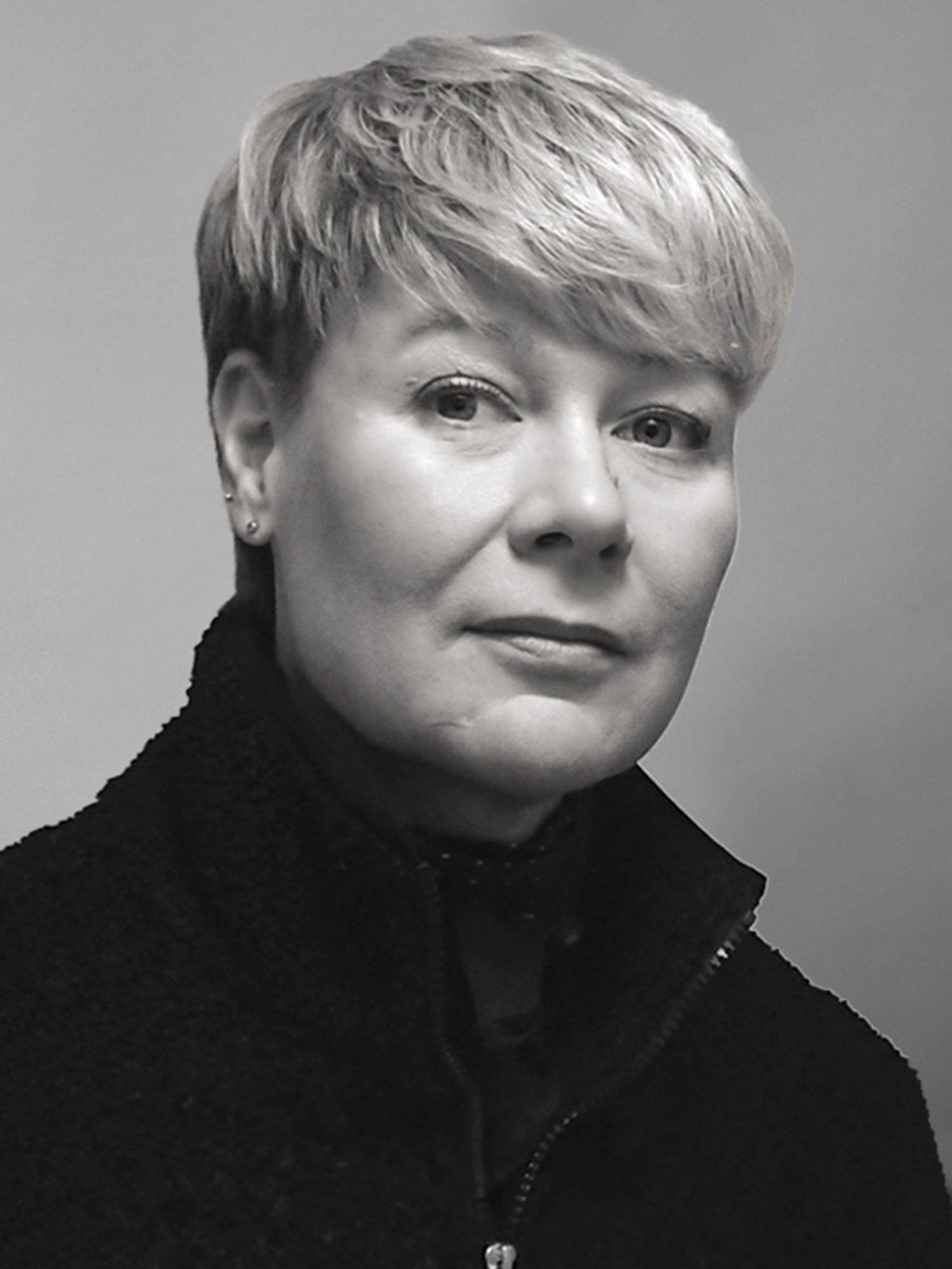 Eine Person mit kurzen, hellen Haaren und einer dunklen Jacke mit Reißverschluss blickt vor einem schlichten Hintergrund in die Kamera.