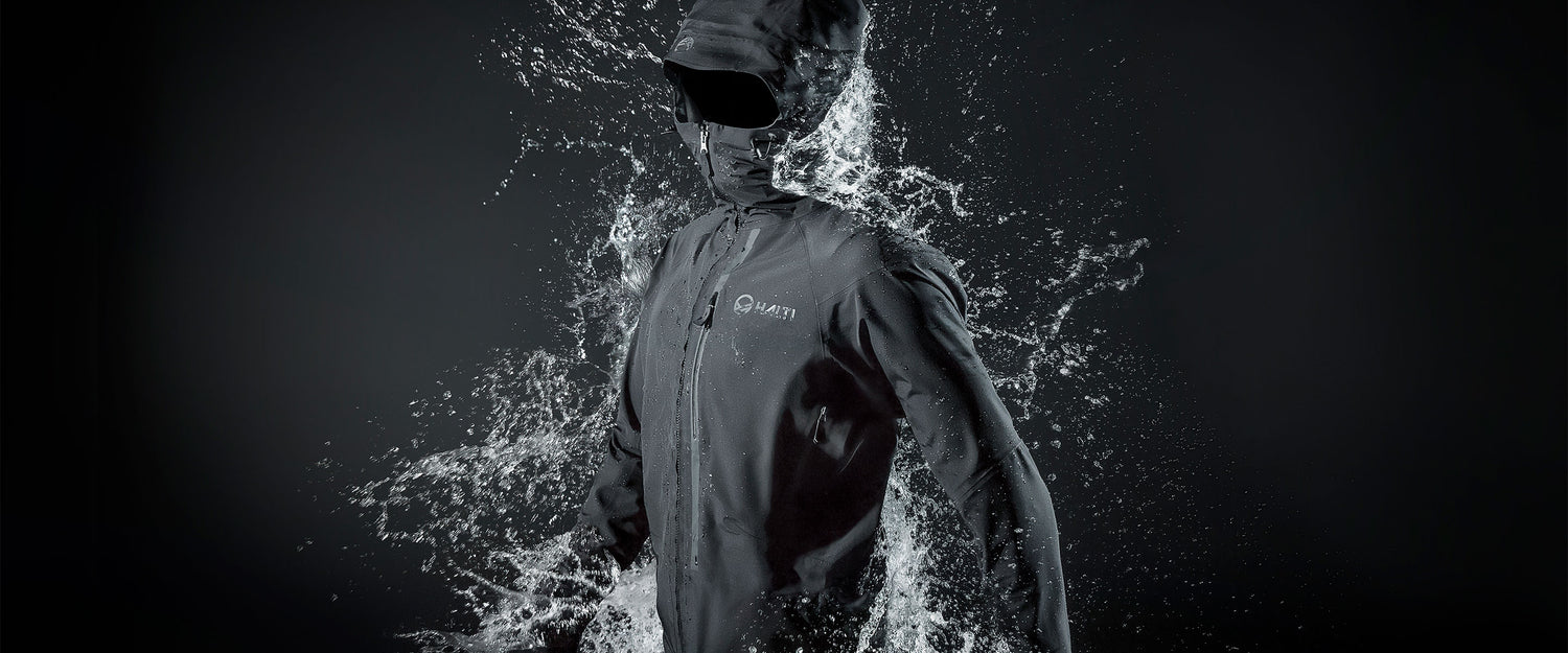 Eine Person, die eine dunkle, wasserdichte Jacke und eine Kapuze trägt, wobei das Wasser dramatisch um ihren Körper spritzt.