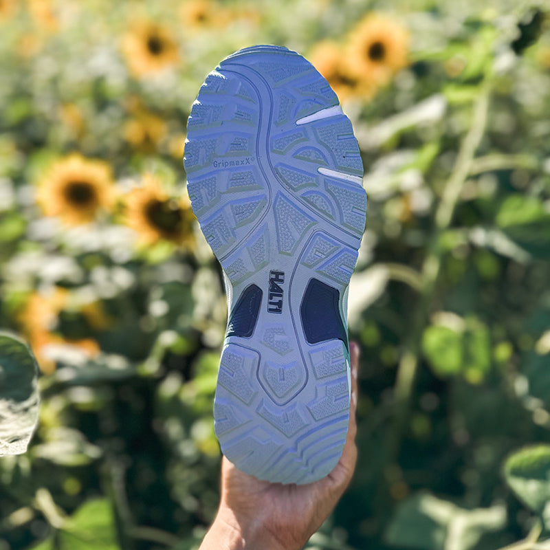 Eine Nahaufnahme einer Halti Fara Damen Low 2 DX Schuhsohle vor Sonnenblumen und grünen Blättern.