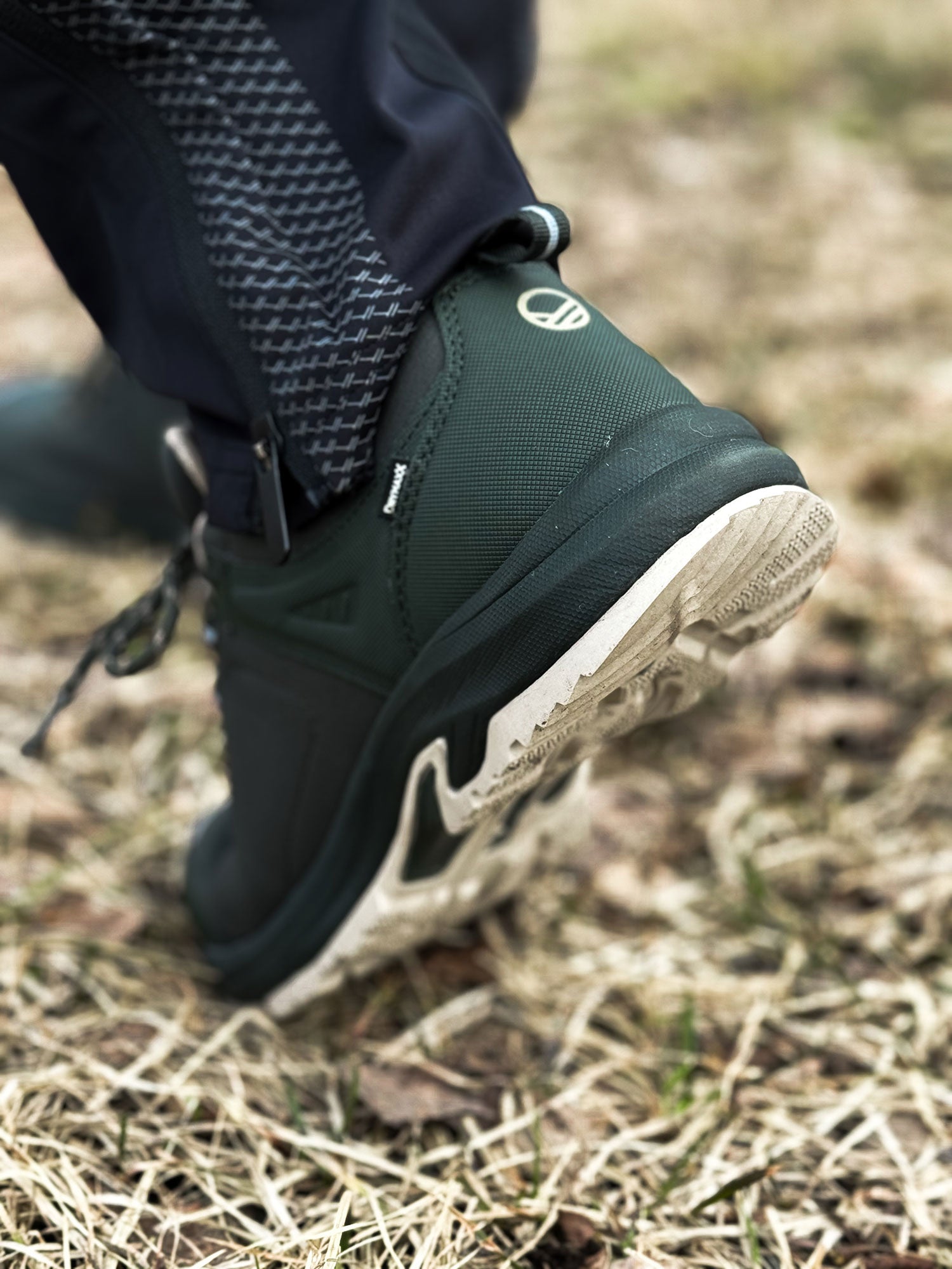 Eine Person in Halti Outdoor-Schuhen Low DX Herren mit GripmaxX Antislip-Sohle tritt auf trockenes Gras, wobei die Sohle sichtbar ist.