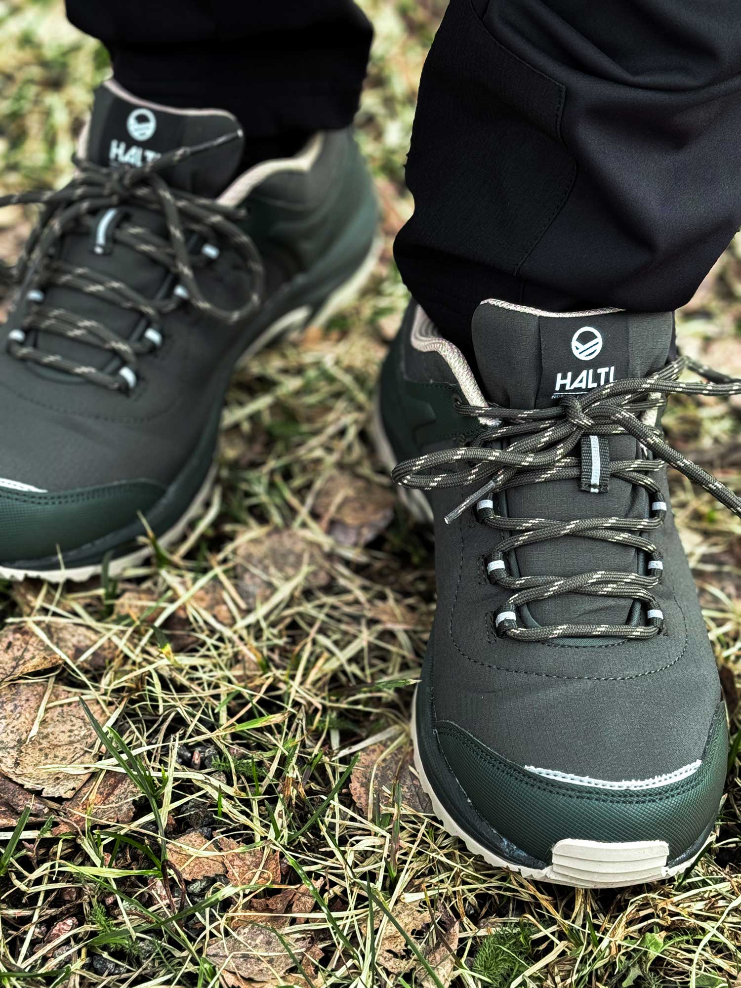 Nahaufnahme einer Person, die Halti Outdoor-Schuhe Low DX Herren mit GripmaxX Antislip-Sohle trägt, auf Gras und trockenem Laub.