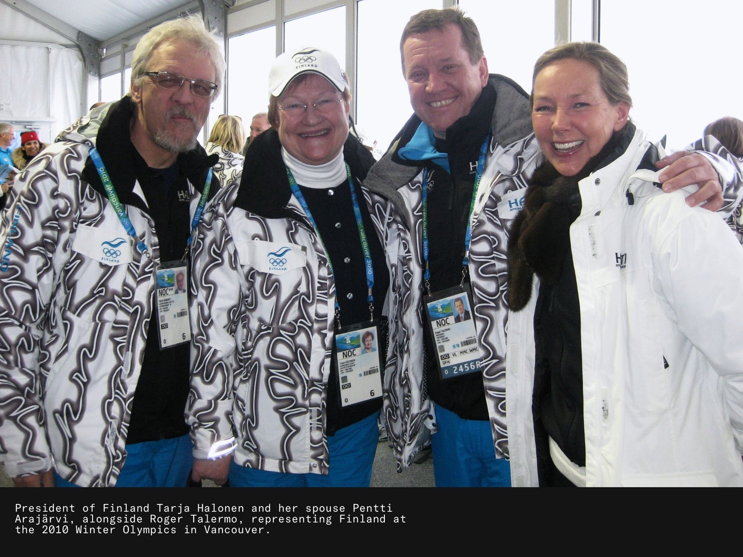Vier Erwachsene in Winterjacken und Mützen lächeln für ein Foto in einer Halle, die wie eine Sportveranstaltung aussieht.