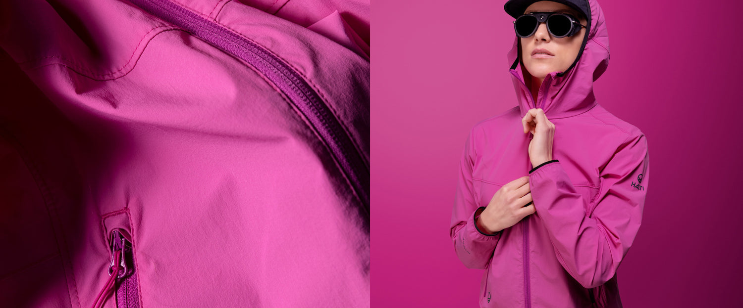 Nahaufnahme des Reißverschlusses einer rosa Jacke neben einer Person, die eine rosa Kapuzenjacke, eine Sonnenbrille und eine Mütze trägt.