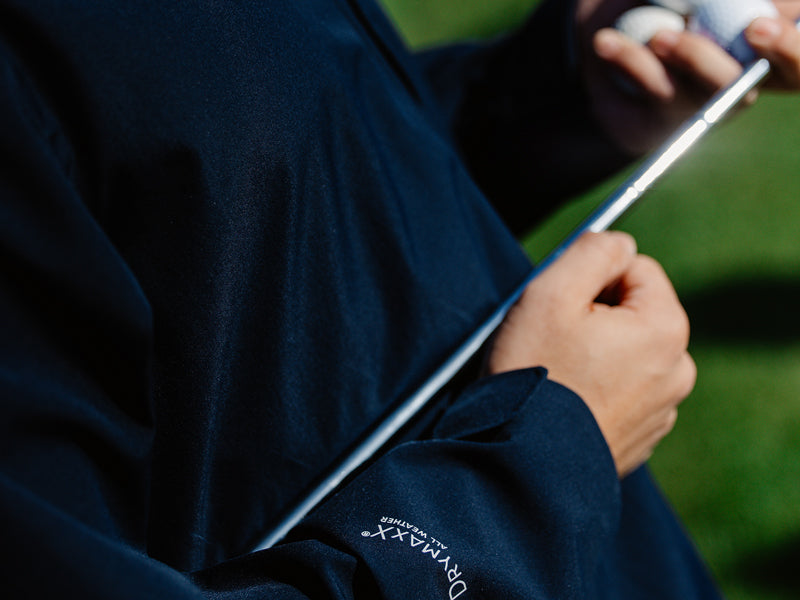 Person, die einen Golfschläger in der Hand hält und eine dunkelblaue Jacke mit der Aufschrift