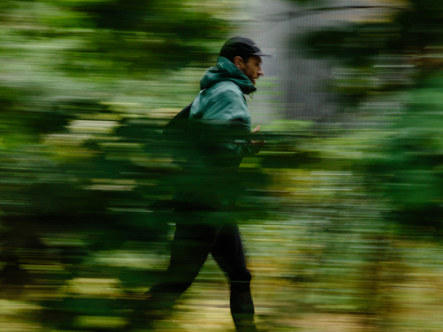 Eine Person, die eine Jacke und eine Mütze trägt, läuft im Freien, aufgenommen in Bewegung mit unscharfem Grün im Vordergrund.