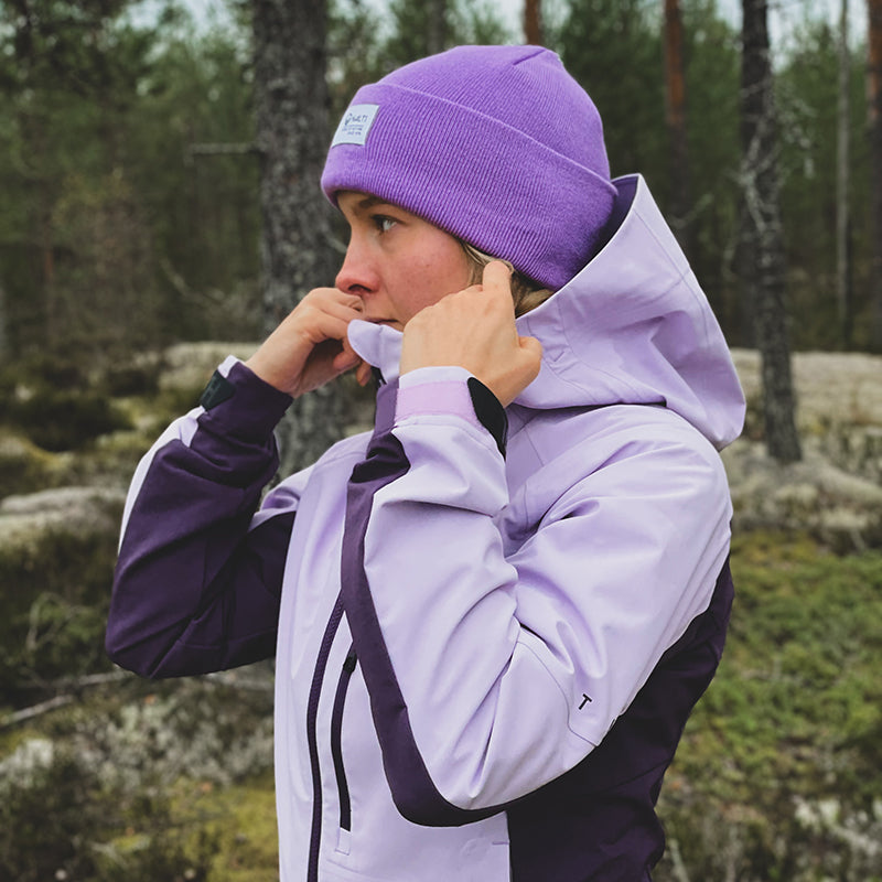 Eine Person mit einer lila Mütze zieht in einem Waldgebiet den Reißverschluss ihrer Halti Pallas III Damen Warm Hybrid Jacke zu.