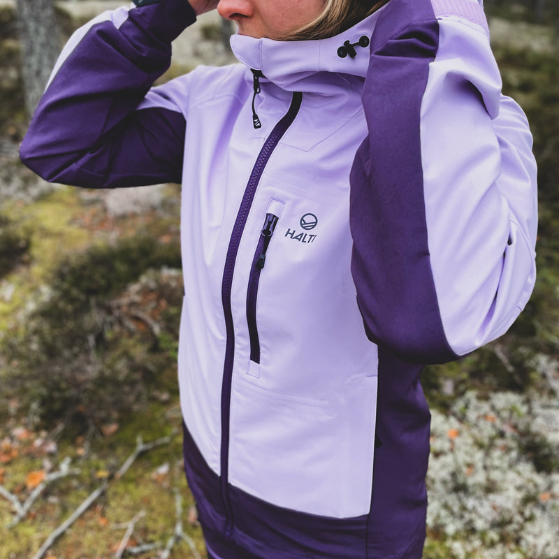 Eine Person in einer lilafarbenen Halti Pallas III Damen Warm Hybrid Jacke passt die Kapuze an und genießt ihren wasserdichten Komfort.
