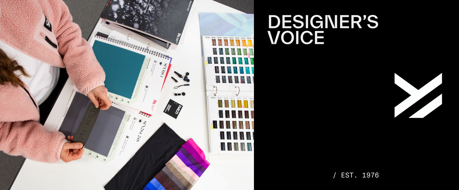 Person in rosafarbenem Pullover begutachtet Farbmuster und Stoffproben auf einem Schreibtisch; Text: