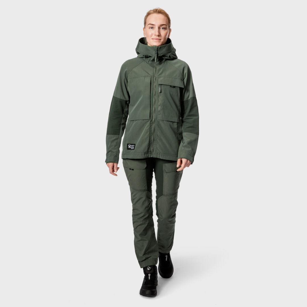 Eine Frau trägt die Halti Hiker Damen Ventilated Jacke mit passenden Hosen und schwarzen Boots vor grauem Hintergrund.