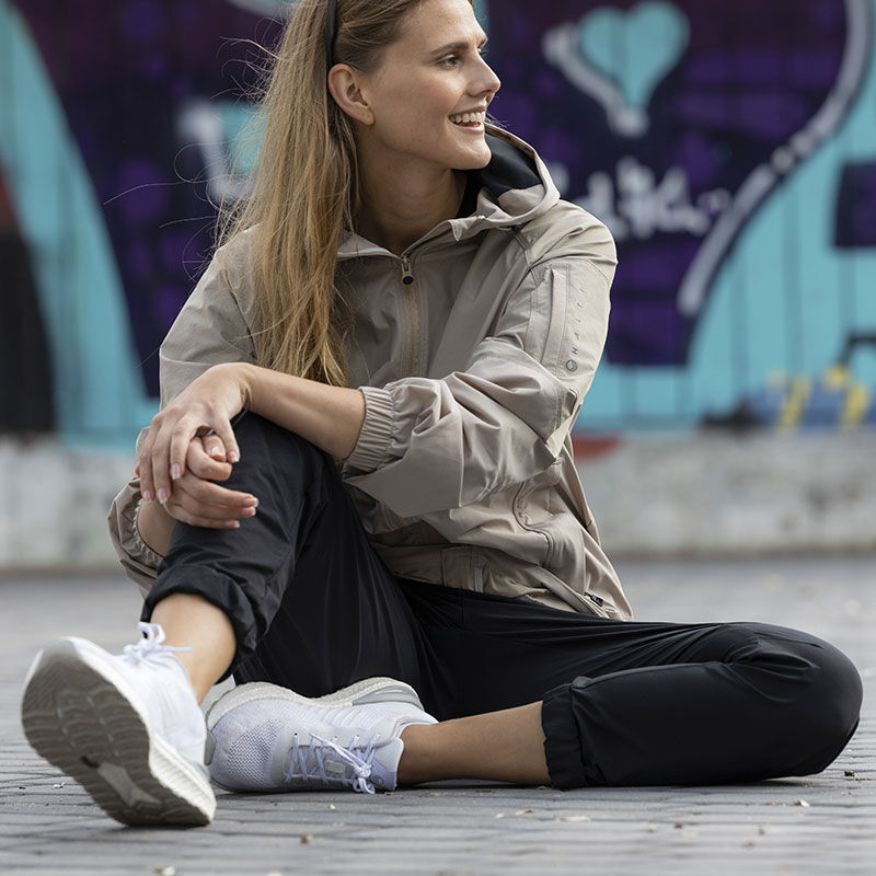 Eine Frau in Halti Gale Sneaker Damen aus atmungsaktivem Recyclingtextil sitzt im Schneidersitz vor einer mit Graffiti bedeckten Wand.