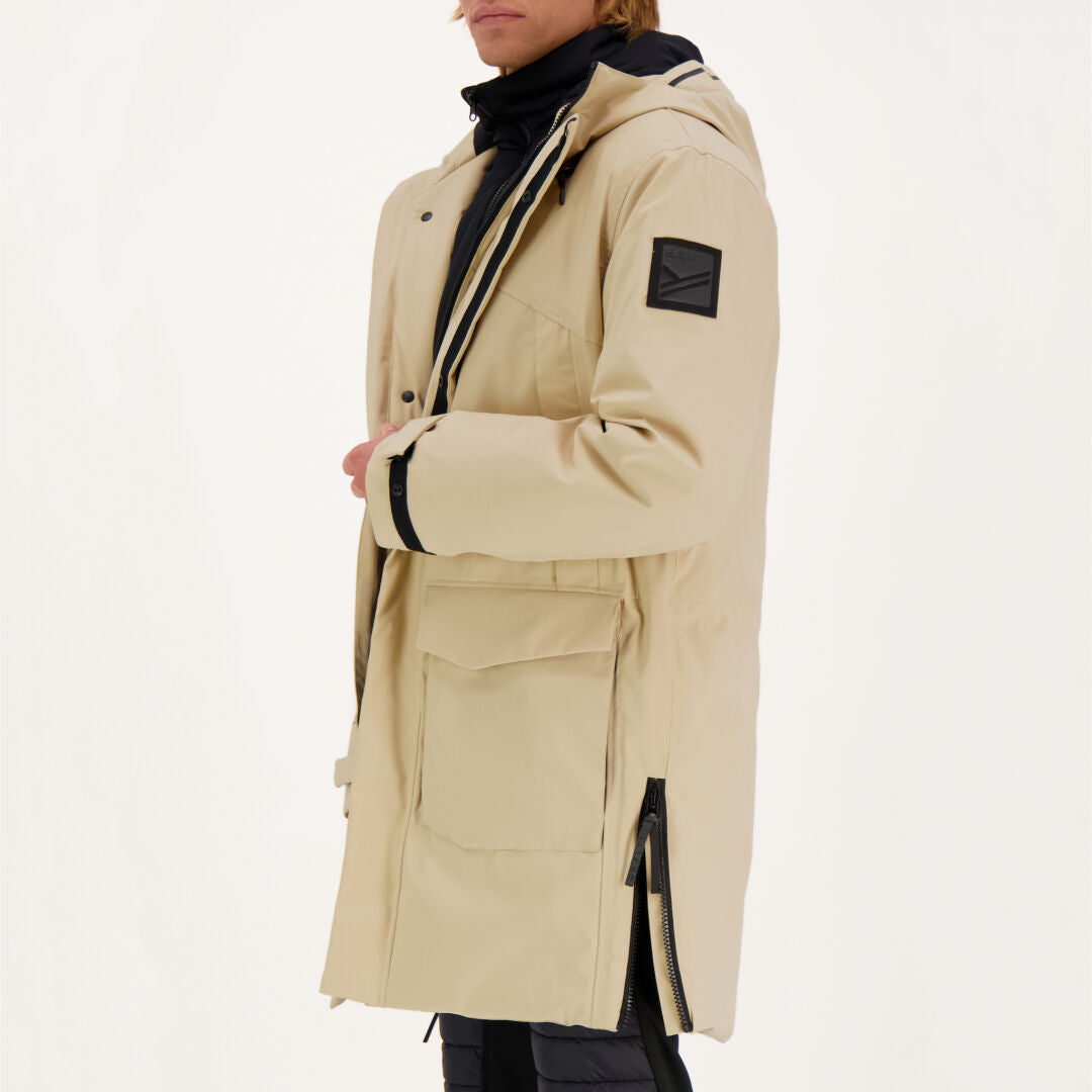 Mann trägt Halti Bergga DX Winter Parka Herren in beige mit schwarzen Details und großer Fronttasche, einfarbiger Hintergrund.