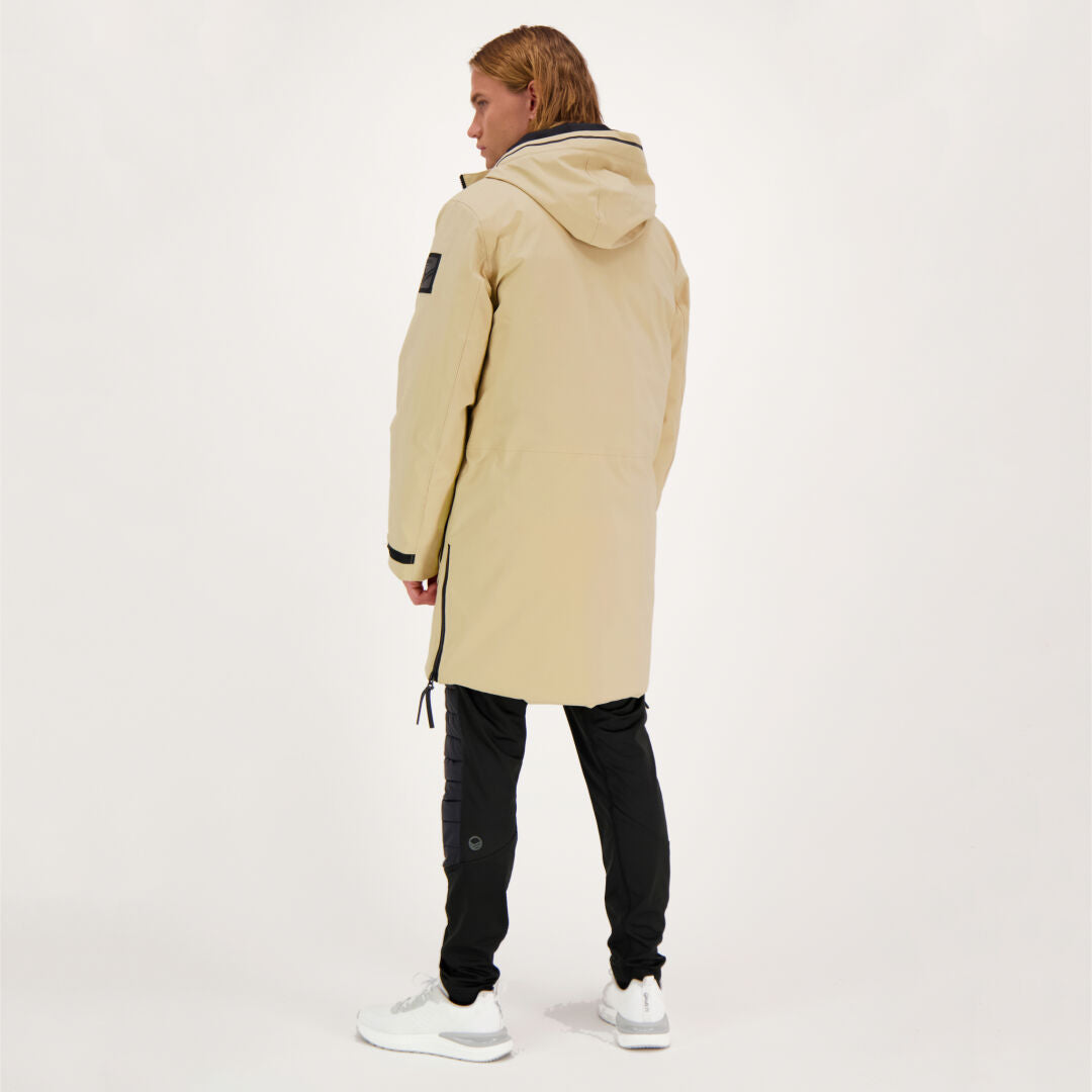 Person steht mit dem Rücken zur Kamera und trägt einen Halti Bergga DX Winter Parka Herren in Beige und eine schwarze Hose.