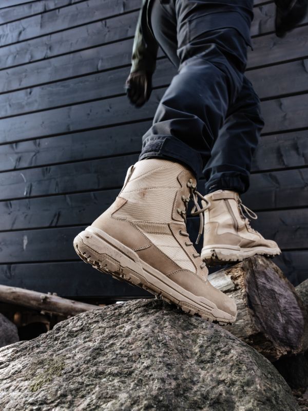 Eine Person, die Halti Regis DX Stiefel Herren und dunkle Hosen trägt, tritt auf große Felsen in der Nähe einer dunklen Holzwand.