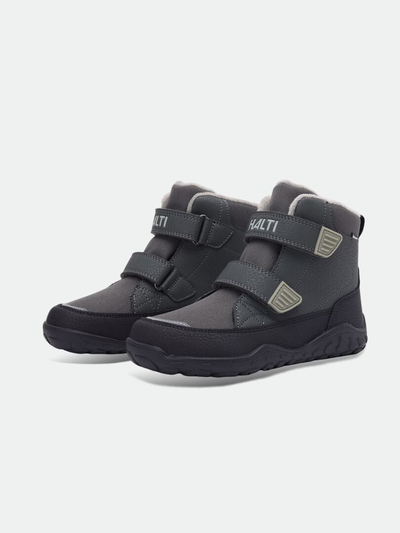 Halti Jalava DX Barfußstiefel für Kinder in Dunkelgrau mit Klettverschlüssen und dicken Sohlen, abgebildet vor einem einfarbigen Hintergrund.