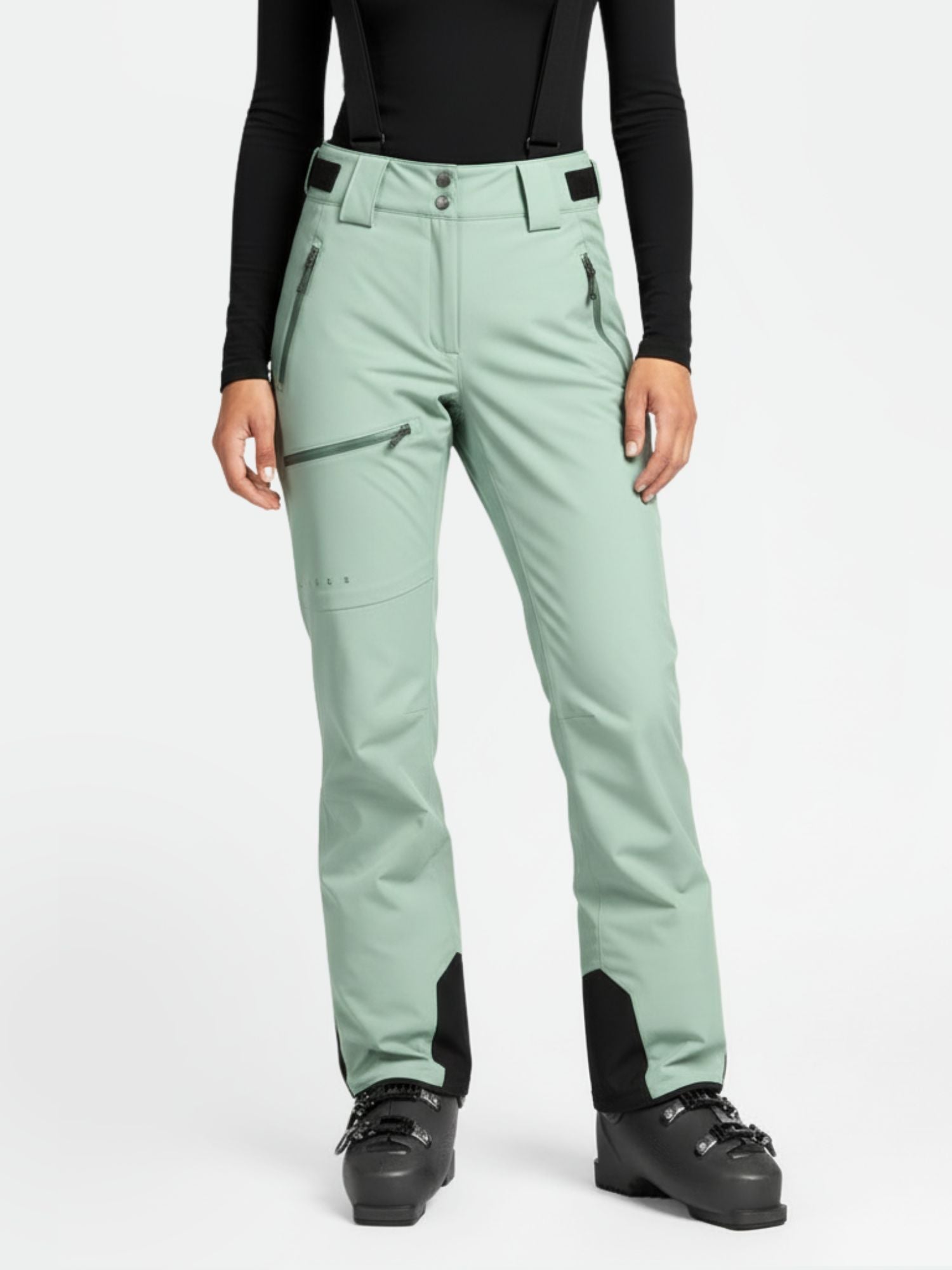 Eine Person in hellgrünen Halti Carvey DX Skihosen Damen, schwarzen Skistiefeln und einem langärmeligen schwarzen Oberteil, Schultern nach unten.