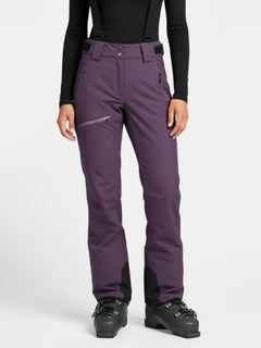 Eine Person in einer lila Halti Carvey DX Skihose Damen mit schwarzen Hosenträgern, schwarzen Stiefeln und einem schwarzen Oberteil steht aufrecht.