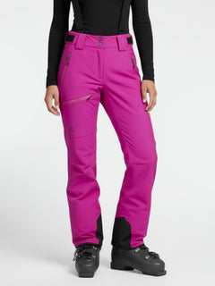 Person trägt Halti Carvey DX Skihose Damen in Magenta, schwarzes langärmeliges Oberteil und Skischuhe auf weißem Hintergrund.