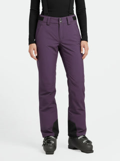 Eine Person in lila Halti Trusty DrymaxX Skihose Damen, schwarzen Hosenträgern, schwarzem Top und Skischuhen auf weißem Hintergrund.