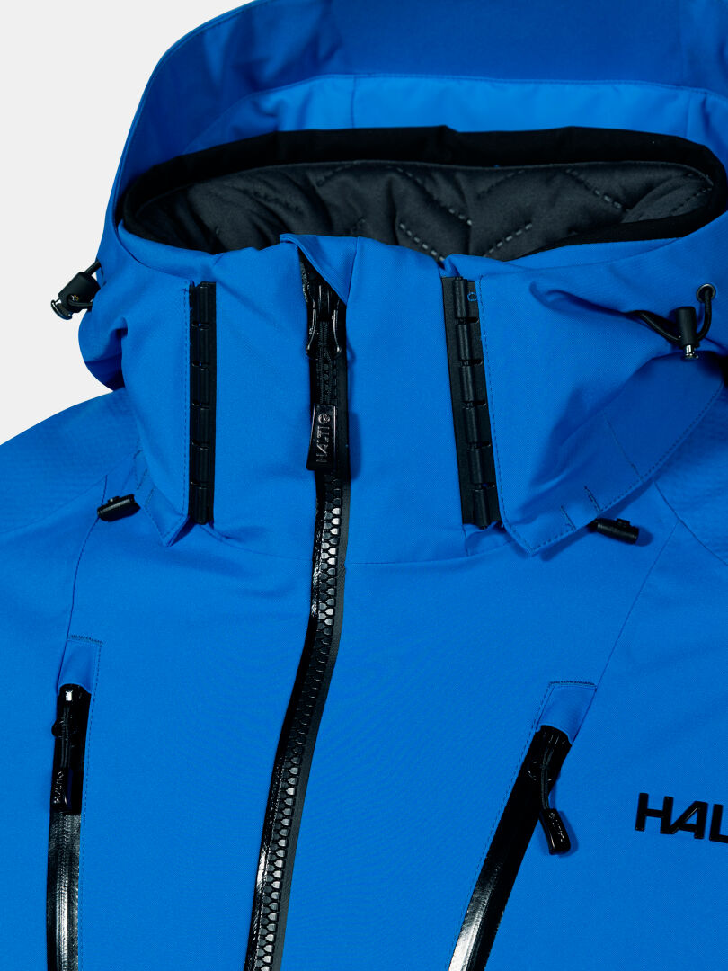 Nahaufnahme einer blauen Vertica DX Skijacke Herren von Halti, mit schwarzen wasserdichten Reißverschlüssen, hohem Kragen und partiellem HAL-Logo.