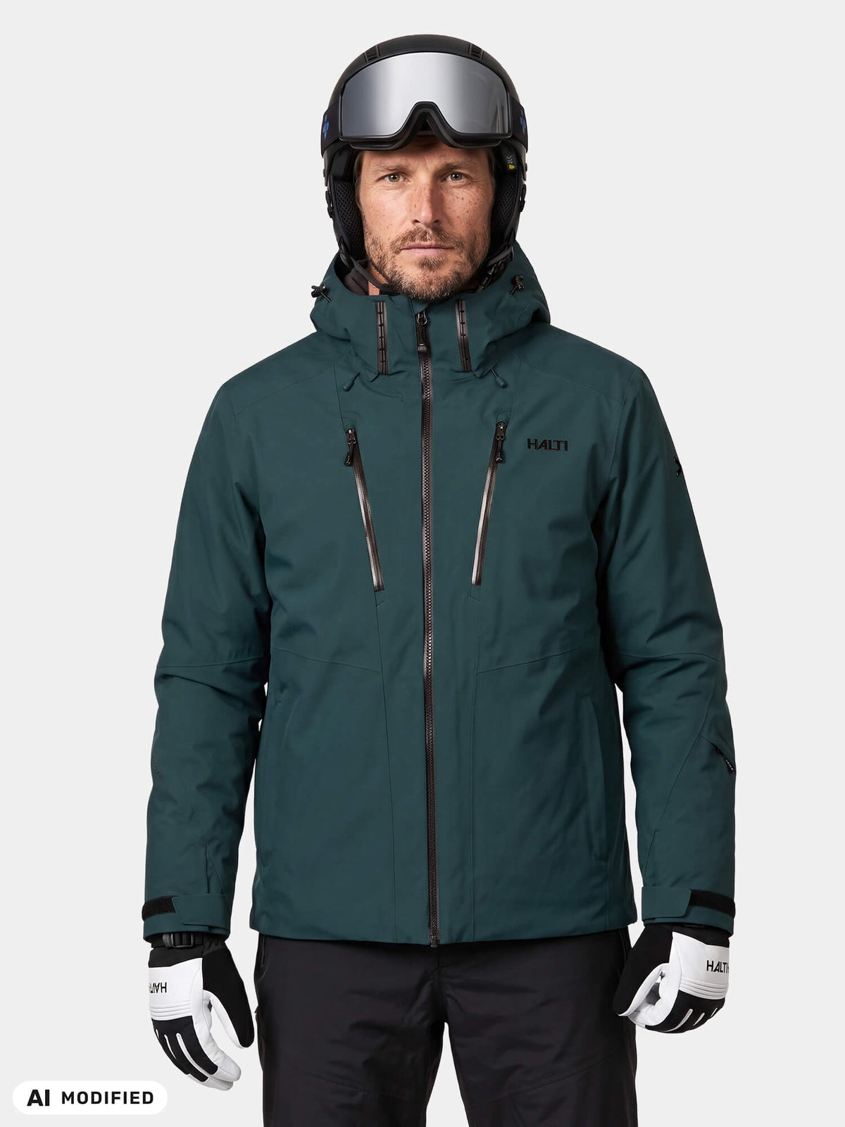 Ein Skifahrer in einer blaugrünen Halti Vertica DX Skijacke für Herren, einer schwarzen Hose, einem Helm und einer Skibrille.
