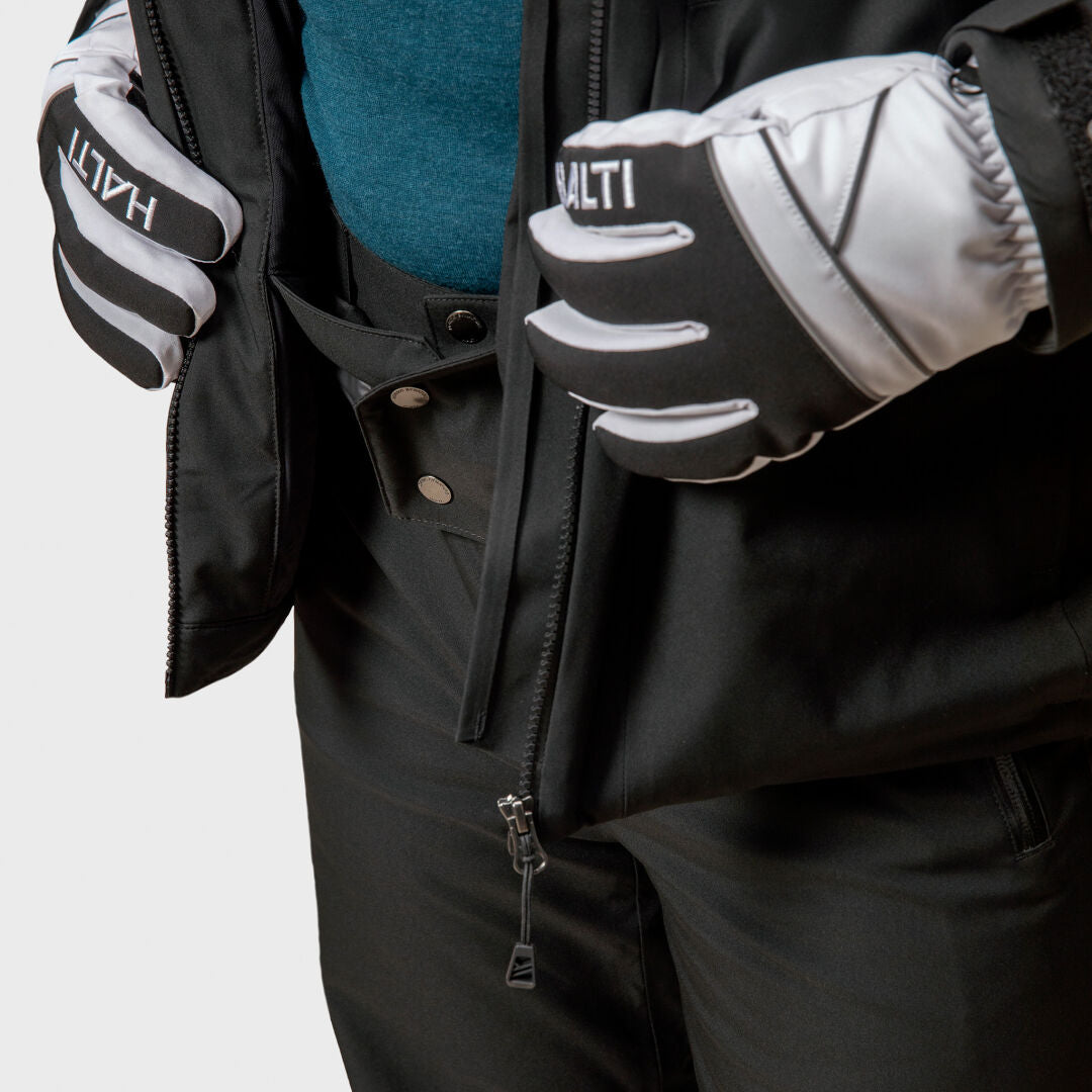 Er trägt eine schwarze Halti Vertica DX Skijacke Herren mit Primaloft Silver und öffnet den Reißverschluss, um ein blaues Hemd darunter zu zeigen.