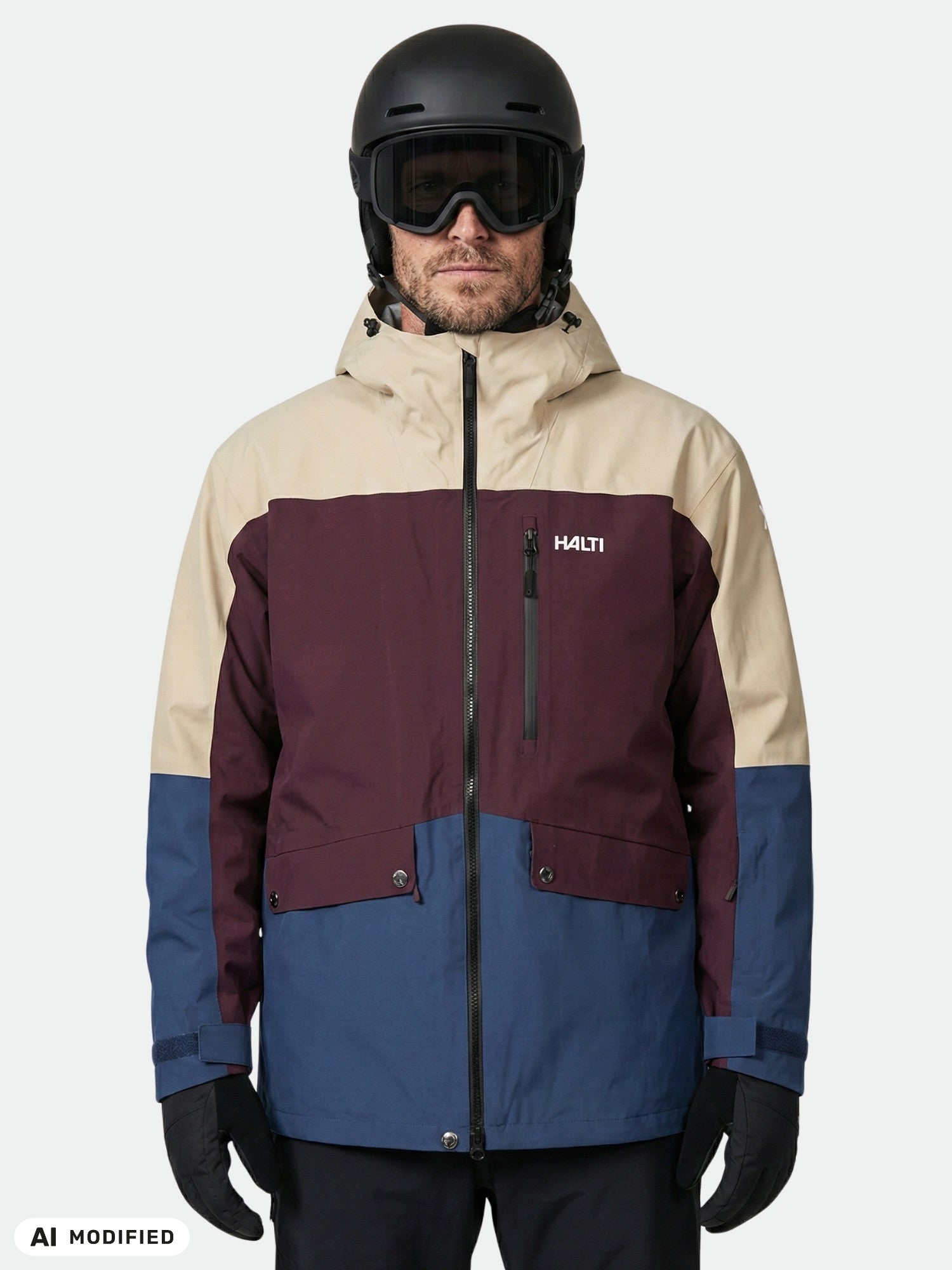 Ein Mann, der eine „Halti Settler 3L DX“ Skijacke für Herren, einen schwarzen Helm und eine Skibrille trägt, blickt vor einem einfarbigen Hintergrund in die Kamera.