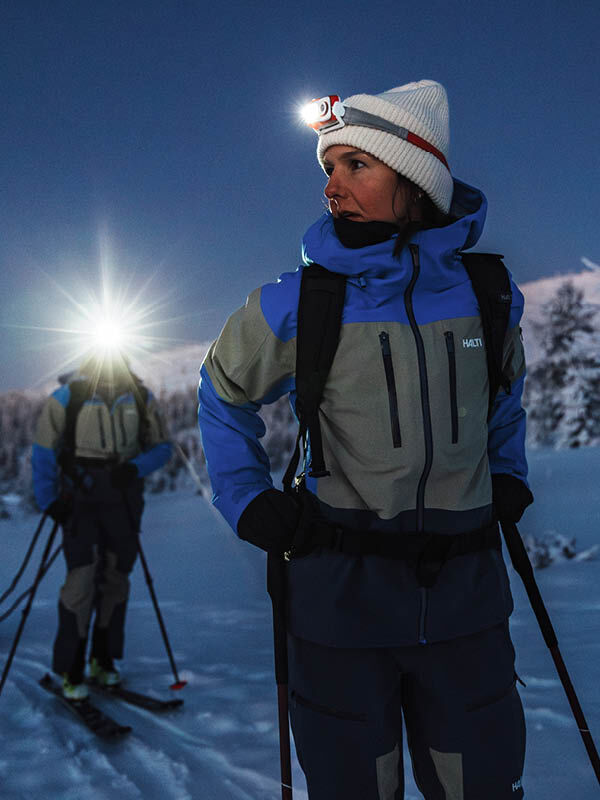 Zwei in Winterkleidung und mit Stirnlampen fahren in der Morgendämmerung Ski - perfekt als Geschenk für eine Halti Geschenkkarte.