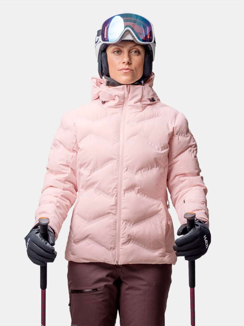 Person in Halti Nordic Arcty II Skijacke Damen, braune Hose, Helm und Brille, hält Skistöcke, Blick nach vorne.