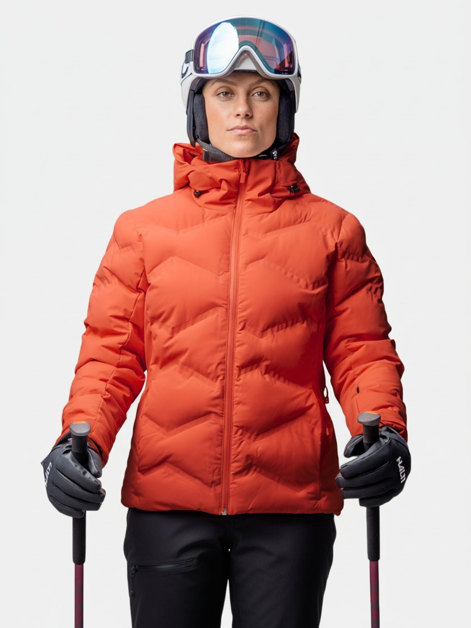 Eine Frau trägt die Halti Nordic Arcty II Skijacke Damen mit Skihelm, Skibrille und Stöcken vor einem schlichten Hintergrund.
