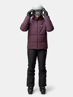 Frau in Halti Ascale Puffer Skijacke Damen, schwarze Skihose, Skihelm und Skibrille vor neutralem Hintergrund.