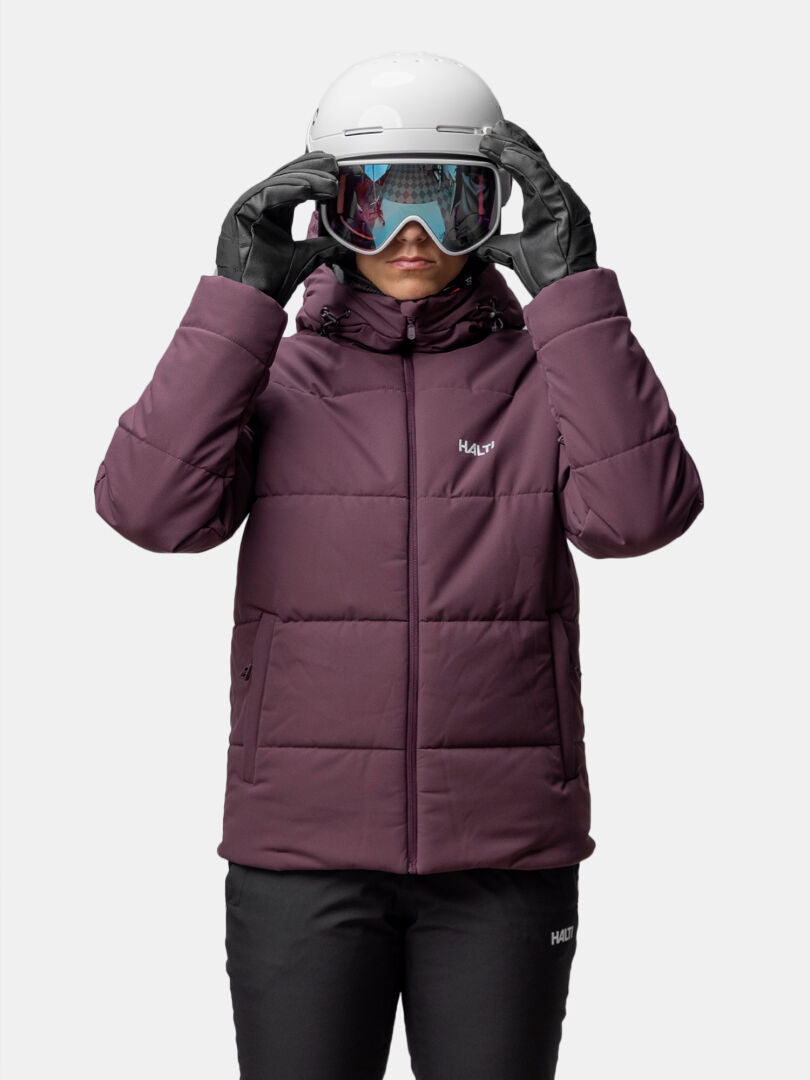 Person trägt eine lila Halti Ascale Puffer Skijacke Damen, eine schwarze Hose, Skihandschuhe, einen Helm und eine Skibrille.