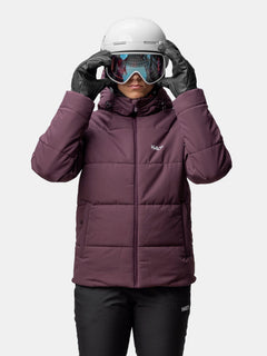 Person trägt eine lila Halti Ascale Puffer Skijacke Damen, eine schwarze Hose, Skihandschuhe, einen Helm und eine Skibrille.